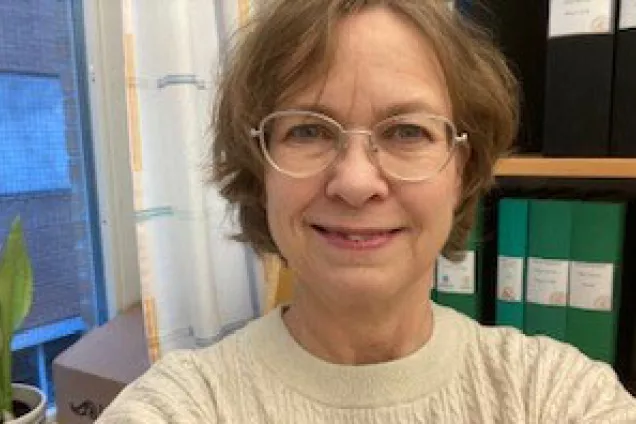 Image of Katarina Turesson in a white knitted sweater standing in her office.