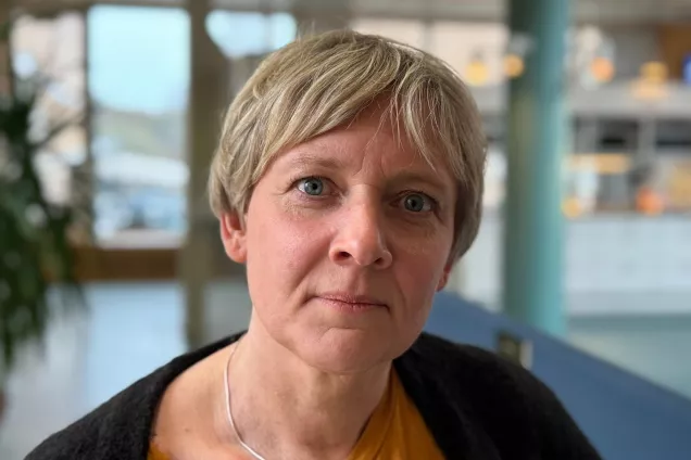 Picture of Caroline Jansson in a corridor area, with short blonde hair and a black knitted sweater.